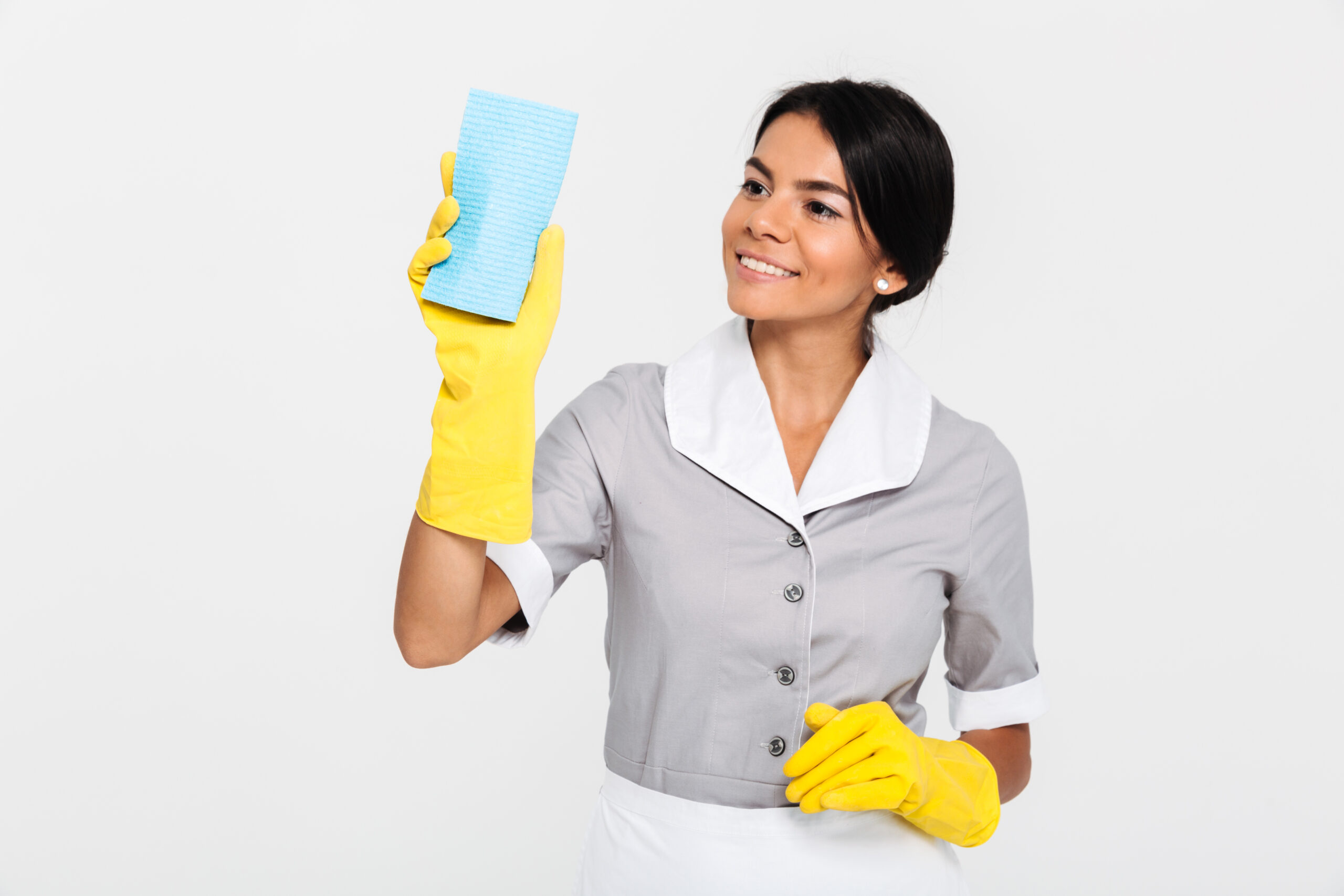 Portrait of a happy pretty housekeeper dressed in uniform cleaning with a sponge while standing isolated over white background